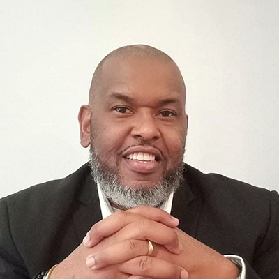 Chiropractor Torey Evans Smiling In A Suit With Hands Clasped